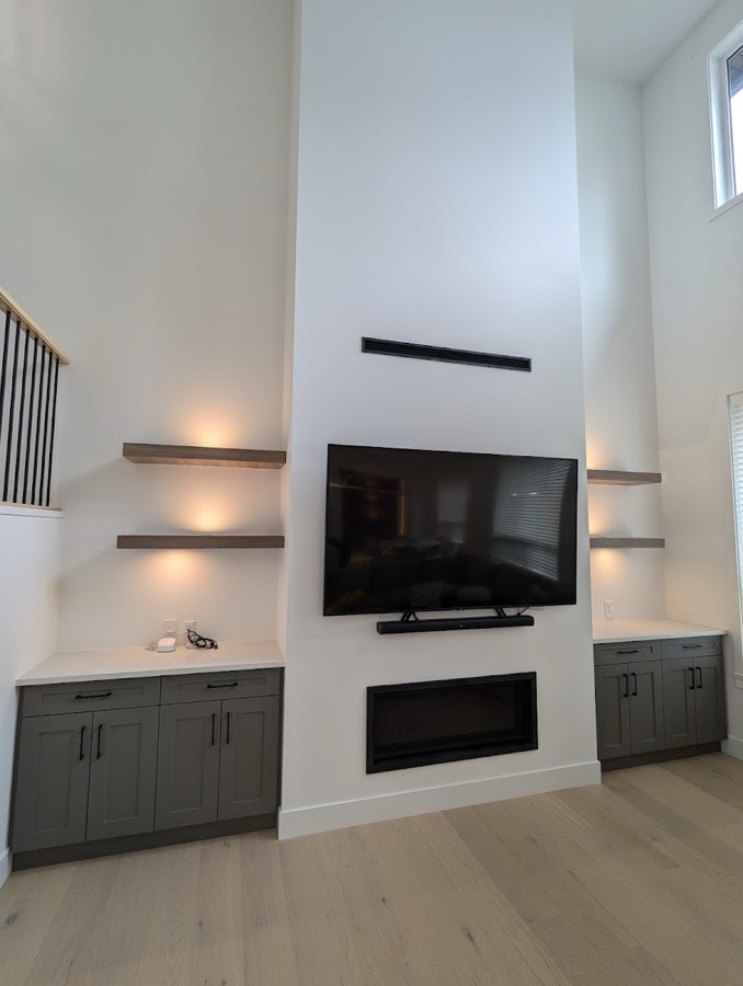 Living room with a wall mounted television, fireplace and lit display shelving